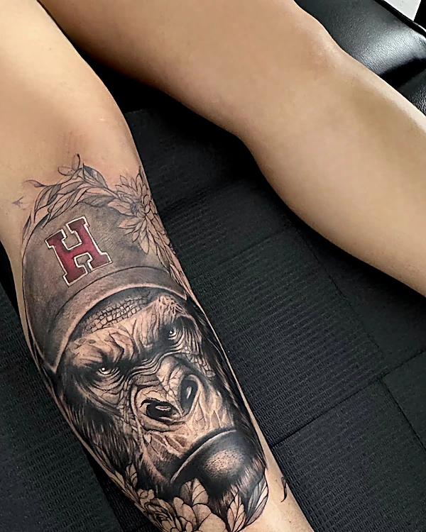 Gorila con gorra de letra H y flores, en negro y gris, en la pantorrilla